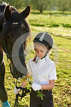 Little girl jockey communicating with her black horse in professional outfit