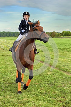 Little girl jockey riding a horse across country in professional outfit