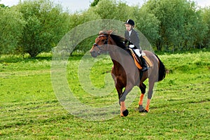 Little girl jockey riding a horse across country in professional outfit