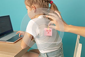 Little girl with joke sticker on back against blue background April fool& x27;s day. date 1 April