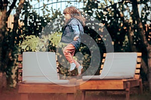 Little Girl Jumping Lounge Chairs Outdoors in the Garden