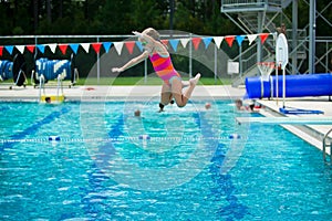 Little girl jumping off the diving board during her swim lessons at the local outdoor pool in the summer