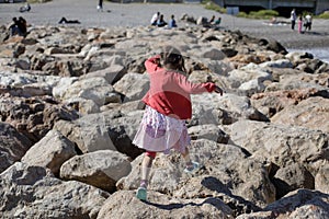 Little girl jumping on rocks on the French riviera during a sunny spring day