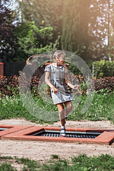Little girl  is jumping on trampoline in a park. Happy laughing kid outdoors in the yard on summer vacation. Jump high