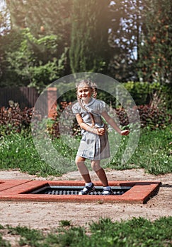 Little girl  is jumping on trampoline in a park. Happy laughing kid outdoors in the yard on summer vacation. Jump high