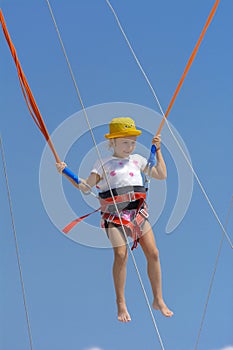 A little girl jumps high on a trampoline with rubber ropes again