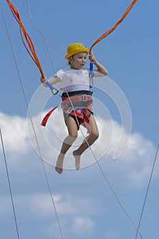 A little girl jumps high on a trampoline with rubber ropes again