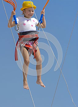 A little girl jumps high on a trampoline with rubber ropes again