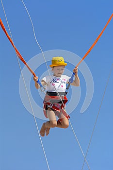 A little girl jumps high on a trampoline with rubber ropes again