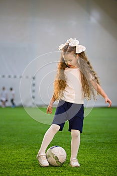 A little girl kicking the ball on the football field playing the game