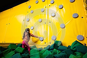 Little girl kid climbing wall at yellow playground park. Child in motion during active entertaiments