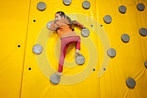 Little girl kid climbing wall at yellow playground park. Child in motion during active entertaiments