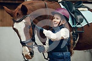 Little girl, kid in helmet taking care after horse, showing her love. Child training horseback riding in special arena