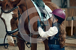 Little girl, kid in helmet taking care after horse, showing her love. Child training horseback riding in special arena