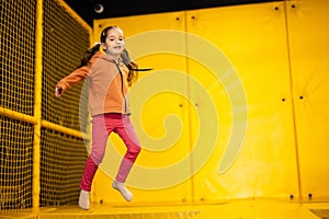Little girl kid jumping on trampoline at yellow playground park. Child in motion during active entertaiments
