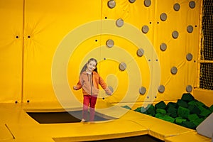 Little girl kid jumping on trampoline at yellow playground park. Child in motion during active entertaiments