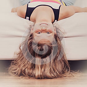 Little girl kid with long hair upside down on sofa