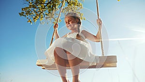 Little girl kid swinging on a wooden swing on a tree in the park. happy family kid dream concept. little kid girl