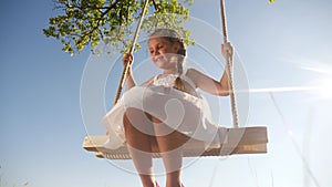 Little girl kid swinging on a wooden swing on a tree in the park. happy family kid dream concept. little kid girl