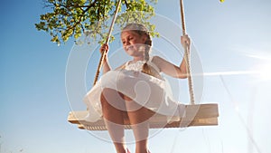 Little girl kid swinging on a wooden swing on a tree in the park. happy family kid dream concept. little kid girl