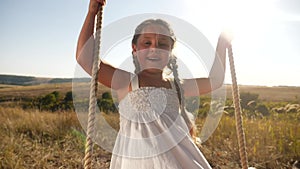 Little girl kid swinging on a wooden swing on a tree in the park. happy family kid dream concept. little kid girl fun