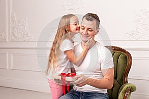 Little girl kiss her father, who hold giftbox in hand, in cheek. Selective focus