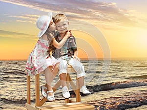 Little girl kissing boy on sea landscape at sunset