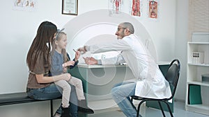 Little girl kissing her mom and smiling male doctor giving her candy for good behaviour