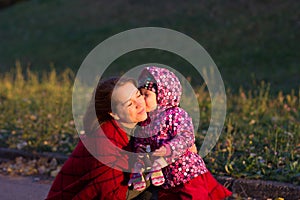 Little girl kissing her mother in autumn park
