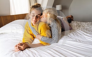 Little girl kissing her mother lying on bed and enjoy the time at home. Mother's Day or mother's love concept image