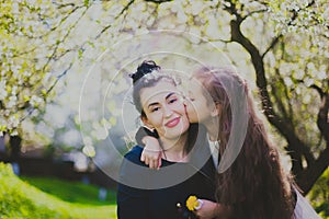 Little girl kissing her mother in the spring cherry garden