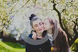 Little girl kissing her mother in the spring cherry garden