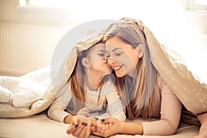 Little girl kissing her mother under blanket