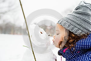 Little girl kissing a snowman in winter nature