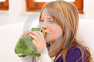 Little girl kissing toy frog on sofa