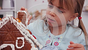 Little girl in the kitchen icing a gingerbread cookie house