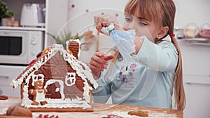 Little girl in the kitchen icing a gingerbread cookie house