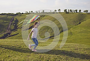 A little girl with a kite runs on a hill on the nature in summer.