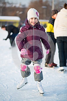 Little girl in knee pads skating at the rink
