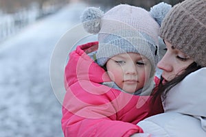 Little girl in a knitted hat with buboes in the arms of a smiling mother on the street in winter photo