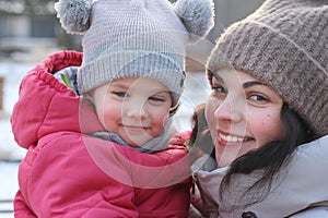 Little girl in a knitted hat with buboes in the arms of a smiling mother on the street in winter photo