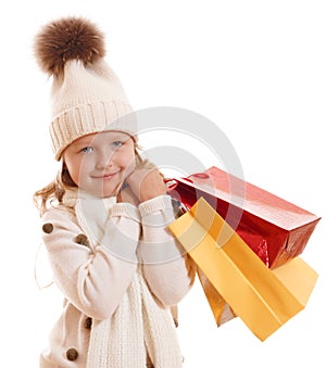 A little girl in a knitted hat with a pompon, scarf and sweater, is holding multicolored paper bags. Isolated on white background