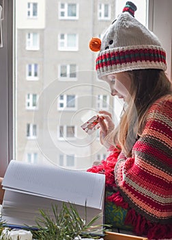 A little girl in a knitted sweater sitting on a windowsill and reading a book