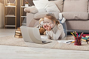 Cute little girl doing homework on laptop, lying on floor