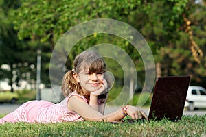 Little girl with laptop lying on grass