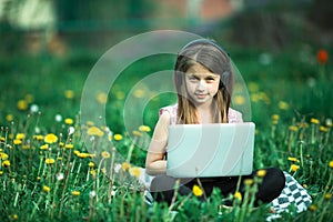 Little girl with laptop lying on the green grass at summer.