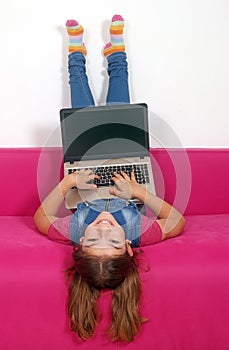 Little girl with laptop lying upside down on bed