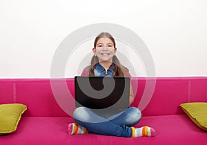 Little girl with laptop sitting on bed