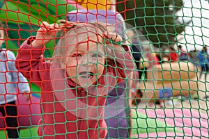 Little girl laughs as she grabs behind a playground net