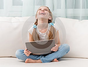 Little girl laughs holding notebook on her crossed legs